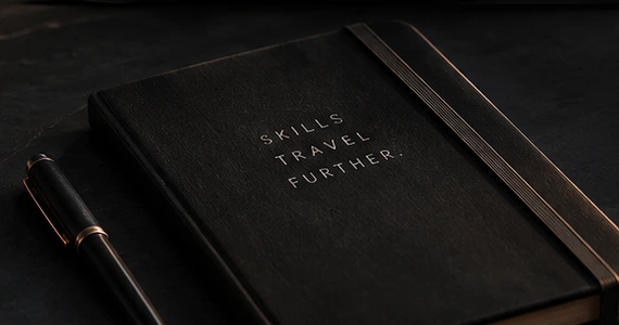 Mørk notesbog med kobberdetaljer og teksten Skills travel further, fra det godkendte MOS-koncept.